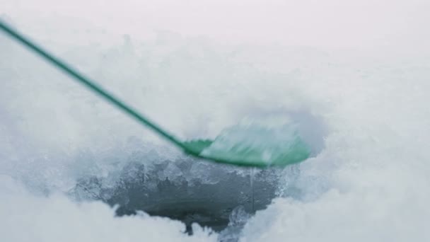 男は、凍った湖で冬の釣りに取り組んでいます。氷の皮の穴をクリアします. — ストック動画