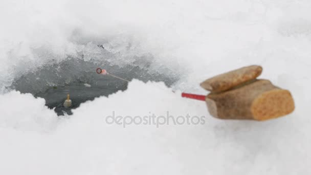 Hengel voor de visserij van de winter in de buurt van het gat in het ijs. De vlotter beweegt door het water — Stockvideo