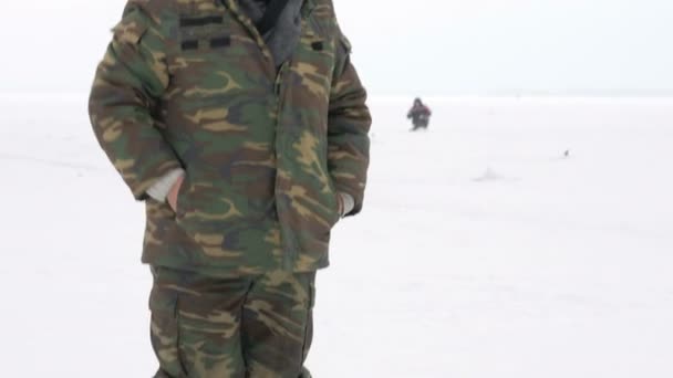 这个人被从事冬季捕鱼。它的成本关于等待鱼的钓鱼杆。热烈穿着防护服 — 图库视频影像