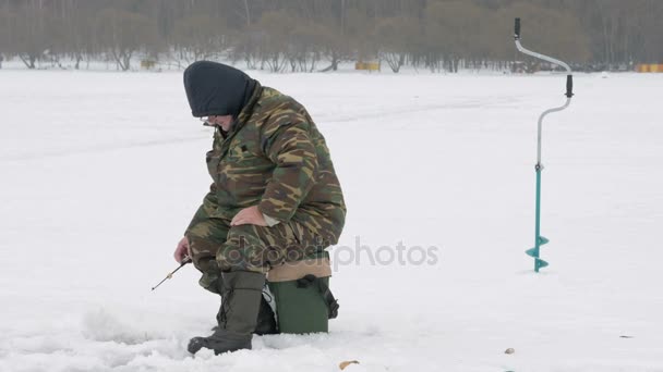 The man is engaged in winter fishing. It costs about fishing rods waiting fish. Warmly dressed in protective clothing