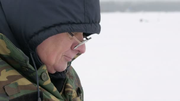 冬の湖で釣り、ポットからお茶を飲む男。彼はホットド リンクとビスケットを食べる — ストック動画