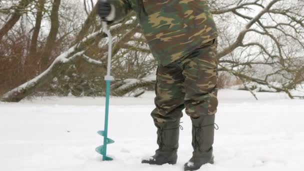 Pesca invernale sul fiume. Un uomo fa un buco nel ghiaccio . — Video Stock