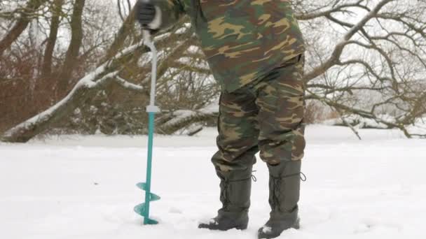 Pêche hivernale sur la rivière. Un homme perce un trou dans la glace . — Video