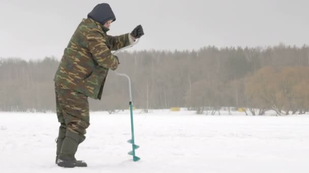 Zimní rybaření na řece. muž vrtáky do ledu díru. — Stock video