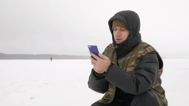 Mladý muž na zamrzlém jezeře s telefonem hledá pro požadovanou trasu. — Stock video