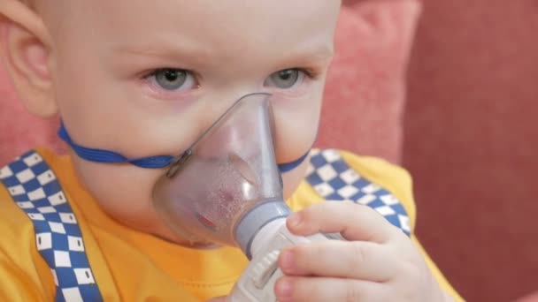 El propio niño sostiene una máscara de un inhalador y respira el medicamento en casa. Trata la inflamación de las vías respiratorias a través del nebulizador. Prevención del asma y la tos . — Vídeo de stock