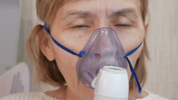 Seniorin mit Maske aus Inhalator zu Hause. behandelt Entzündungen der Atemwege mittels Vernebler. Prävention von Asthma und Husten — Stockvideo