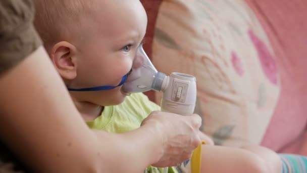 Η μητέρα κρατά τη μάσκα της συσκευής εισπνοής μωρό και αναπνέει το φάρμακο στο σπίτι. Αντιμετωπίζει τη φλεγμονή των αεραγωγών μέσω νεφελοποιητή. Πρόληψη του άσθματος και βήχα — Αρχείο Βίντεο