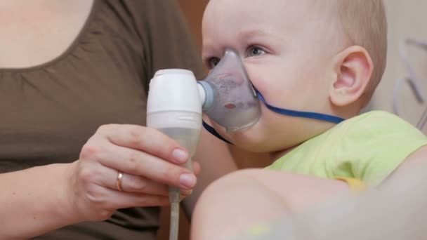 Η μητέρα κρατά τη μάσκα της συσκευής εισπνοής μωρό και αναπνέει το φάρμακο στο σπίτι. Αντιμετωπίζει τη φλεγμονή των αεραγωγών μέσω νεφελοποιητή. Πρόληψη του άσθματος και βήχα — Αρχείο Βίντεο