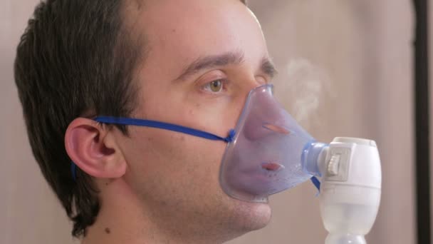 Νεαρός άνδρας κρατά στο σπίτι μια μάσκα από μια συσκευή εισπνοής. Αντιμετωπίζει τη φλεγμονή των αεραγωγών μέσω νεφελοποιητή. Πρόληψη του άσθματος και βήχα — Αρχείο Βίντεο