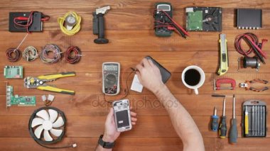 Bir cep telefonu tamir adam. Cihazın içinde parça denetler. Ahşap masa üstü görünümü.