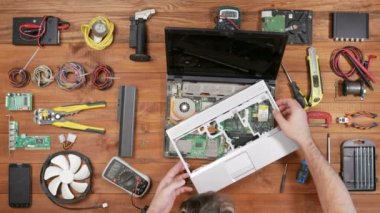 Bir adam bir multimetre ile bir dizüstü bilgisayar ayrıntılarını denetler. Demonte bilgisayar, bir ahşap masa üstü görünümü. İlgili kişileri dokun ve okuma kontrol