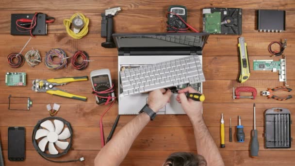 Мужчина-инженер при ремонте компьютера прикрепляет клавиатуру. Вид сверху на деревянный стол — стоковое видео