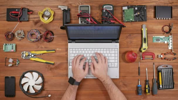 Чоловічий інженер друкує для ноутбука і перевіряє повідомлення на смарт-годиннику. Вид зверху дерев'яного столу — стокове відео