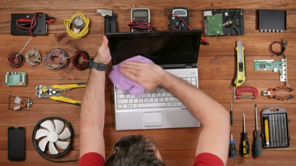 Een man maakt een laptop met een doek schoon na reparaties tegen stof en vuil. Houten tafelblad weergave — Stockvideo