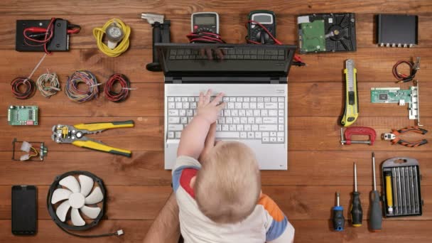Παιδί κάθεται με τον πατέρα του για την επισκευή του υπολογιστή στο χώρο εργασίας και πατήστε τα πλήκτρα σε ένα φορητό υπολογιστή. Ξύλινο τραπέζι κορυφαία προβολή — Αρχείο Βίντεο