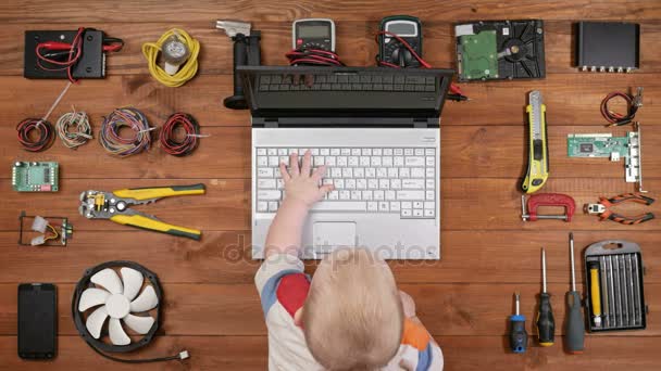 Niño sentado con su padre para la reparación de la computadora del lugar de trabajo y pulse las teclas de un ordenador portátil. Mesa de madera vista superior — Vídeos de Stock