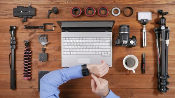 Handen mannelijke fotograaf Controleer berichten op smartwatch op een houten tafel. Bekijk van bovenaf. Op de tafel zijn accessoires voor het schieten — Stockvideo