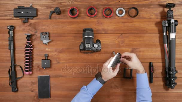 Man fotograaf Led licht verlicht camera en schiet op telefoon. Houten tafelblad weergave. Uitrusting voor het fotograferen op tafel — Stockvideo