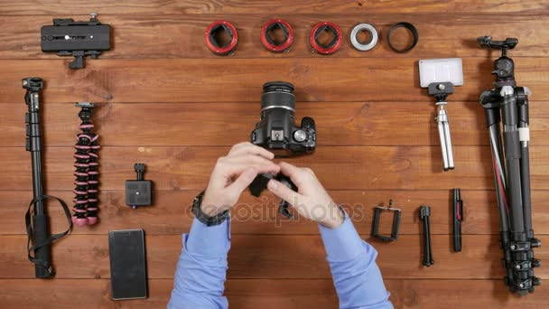 Handen mannelijke fotograaf zet de camera op de bal hoofd. Elk been wordt geopend en gesloten. Houten tafelblad weergave. Uitrusting voor het fotograferen op tafel — Stockvideo