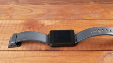 Siyah akıllı saat ahşap bir masada yatıyor. Kurulları tarafından görülebilir. Hareketli kamera