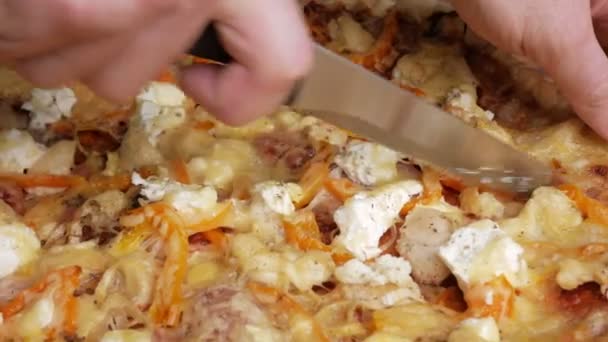 Ein Mann schneidet von Hand ein Stück hausgemachte Pizza mit verschiedenen Käsesorten und Tomaten. bewegliche Kamera — Stockvideo