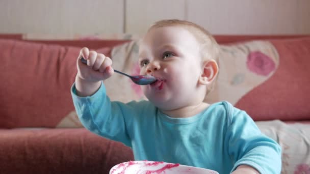 Bir çekici çocuk 2 yaşında bir kırmızı pancar salatası yiyor. Yüz püresi ile sürülür. Masaya oturur. — Stok video