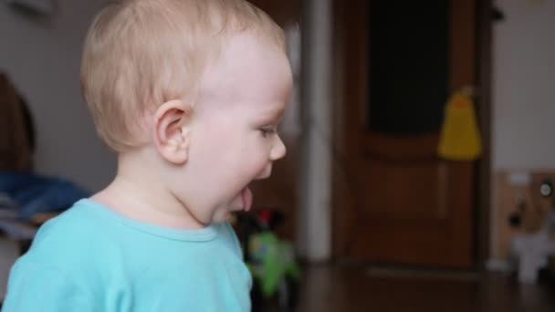 Aantrekkelijke 2-jarige jongen kijkt naar de camera en glimlach en verandert van gezichtsuitdrukkingen. Woninginrichting. Blauw T-shirt. — Stockvideo