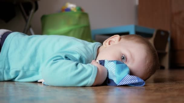 An attractive boy 2 years old is lying on the floor on clothes. He rests after playing at home. — Stock Video