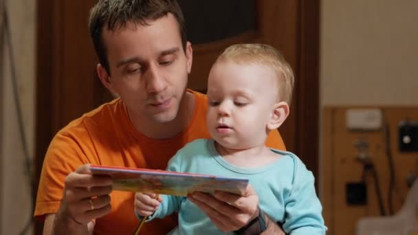 Un ragazzo attraente di 2 anni e papà ha letto un libro a casa. Papà mostra le foto e il figlio chiama gli animali . — Video Stock
