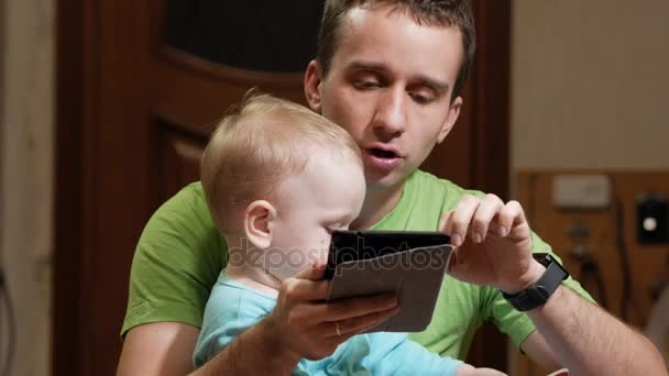Un chico atractivo de 2 años y padre leyeron un libro en casa. Papá muestra las fotos y el hijo llama a los animales . — Vídeo de stock