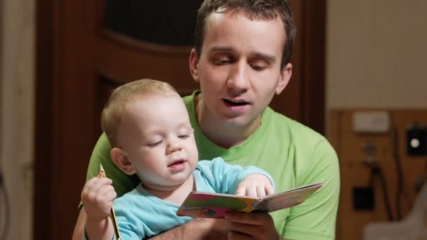 Un chico atractivo de 2 años y padre leyeron un libro en casa. Papá muestra las fotos y el hijo llama a los animales . — Vídeos de Stock