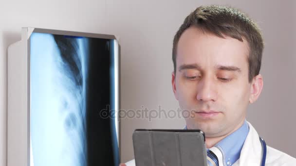 Een jonge dokter maakt gebruik van een tablet-pc in de kliniek. Een man legt de resultaten van een x-ray van de patiënten. — Stockvideo