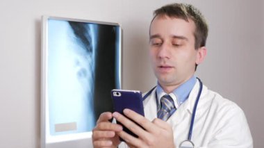 Genç bir doktor klinikte bir telefon kullanır. Bir erkek bir hasta röntgen sonuçları kaydeder.