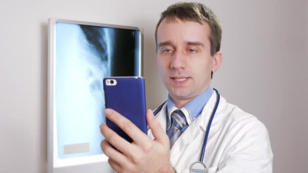 Mladý lékař konzultuje pacienta prostřednictvím Internetu. Video komunikace zobrazuje výsledek pacientů rentgenové a předepisuje léčbu — Stock video