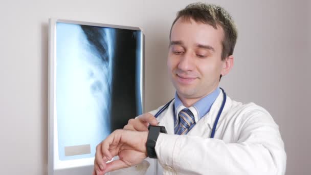 Un médico joven usa un reloj inteligente en la clínica. El hombre dicta los resultados de la radiografía de los pacientes . — Vídeo de stock