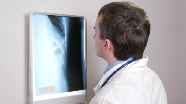 Een jonge dokter onderzoekt de resultaten van een patiënten X-ray op de muur. Analyseert van de borstkas en ribben. — Stockvideo
