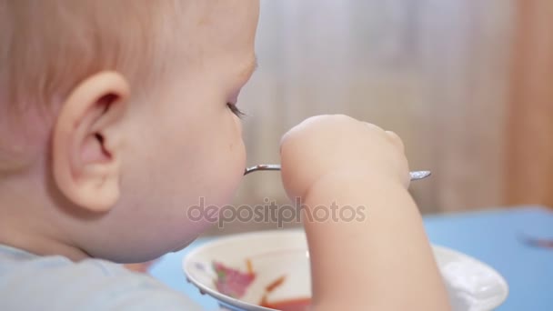 Un ragazzo attraente di 2 anni sta mangiando la zuppa rossa lui stesso. Cucchiaio e mani che scorrono liquido. Il concetto di alimentazione sana dei bambini . — Video Stock