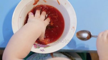 Çekici bir oğlan 2 yaşında kırmızı çorba kendisi yiyor. Plaka elinde tırmanıyor. Tablo Üstten Görünüm.