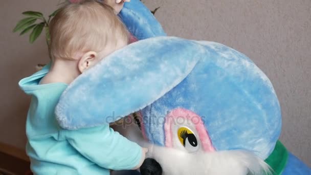 An attractive boy 2 years old plays with a huge plush rabbit at home. Kid shows eyes and touches the ears — Stock Video