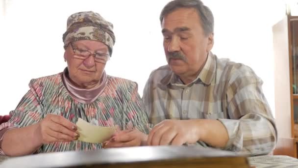 Bir yaşlı çift erkek ve kadın evde onların eski fotoğraflarına bakmaktan ve konuşuyor. Bir bıyık, gözlüklü bir karısı olan bir adam — Stok video