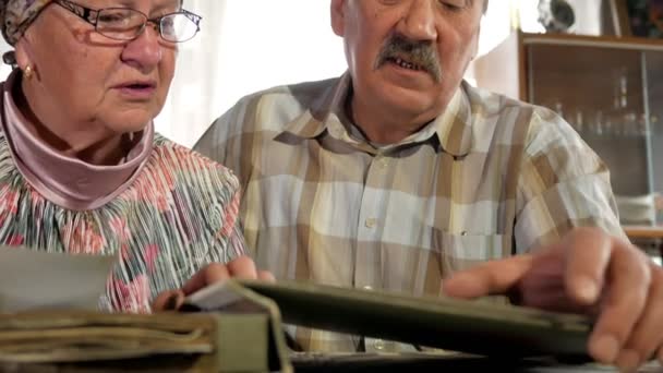 Una pareja de ancianos hombre y mujer están mirando sus viejas fotos en casa y hablando. Un hombre con bigote, una esposa con gafas — Vídeos de Stock