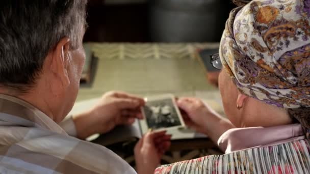 Una coppia anziana uomo e donna stanno guardando le loro vecchie foto a casa e parlano. Un uomo con i baffi, una moglie con gli occhiali — Video Stock