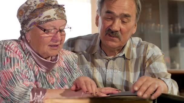 Пожилая пара мужчина и женщина смотрят на свои старые фотографии дома и разговаривают. Мужчина с усами, жена в очках — стоковое видео