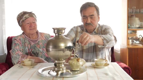 An elderly couple prepares tea with a vintage Russian kettle samovar. A man with a mustache pours tea for his wife — Stock Video