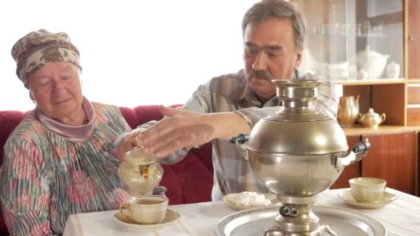 Una pareja de ancianos prepara el té con un samovar hervidor ruso vintage. Un hombre con bigote sirve té para su esposa. — Vídeos de Stock