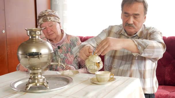 Una pareja de ancianos prepara el té con un samovar hervidor ruso vintage. Un hombre con bigote sirve té para su esposa. — Vídeos de Stock