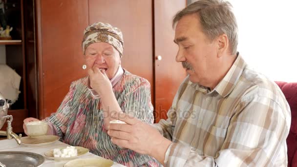 Пожилая пара пьет чай из старинного русского чайника самовара. Мужчина с усами разговаривает с женой в платке — стоковое видео