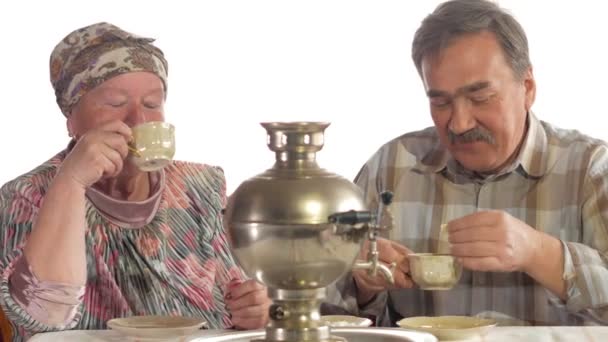 An elderly couple is drinking tea from a vintage Russian kettle samovar. A man with a mustache talking with his wife in a kerchief — Stock Video