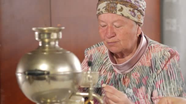 Una pareja de ancianos está bebiendo té de un samovar hervidor ruso vintage. Un hombre con bigote hablando con su esposa en un pañuelo — Vídeo de stock